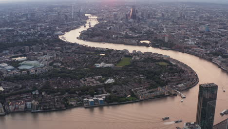 Aerial-panoramic-footage-of-Thames-river-winding-through-town.-Tilt-up-reveal-of-cityscape-in-sunset-time.-London,-UK