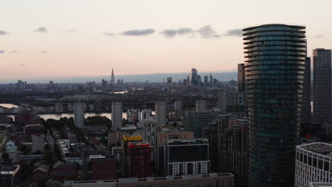 Forwards-fly-around-Arena-Tower-skyscraper-of-Isle-of-Dogs.-panoramic-view-of-cityscape-against-bright-sky-after-sunset.-London,-UK