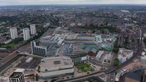 Aerial-panoramic-view-of-huge-modern-shopping-mall.-Urban-neighbourhoods-of-large-city-in-background.-London,-UK