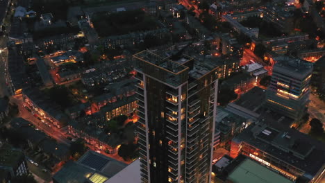 Tilt-down-footage-of-One-The-Elephant-tall-apartment-house.-Modern-high-rise-buildings-against-development-in-urban-neighbourhood-at-night.-London,-UK
