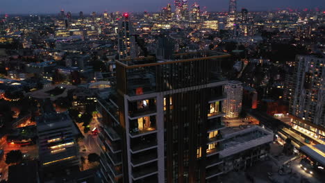 Descending-footage-of-top-floors-of-One-The-Elephant-apartment-building.-Tilt-up-revealing-night-city-panorama.-London,-UK