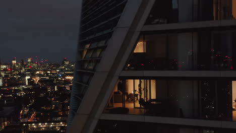 Imágenes-Ascendentes-Nocturnas-De-Un-Edificio-De-Apartamentos-De-Lujo-De-Gran-Altura.-Revelador-Panorama-De-La-Ciudad-Con-Ventanas-Brillantes-De-Los-Rascacielos-Del-Centro.-Londres,-Reino-Unido