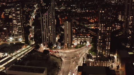 Slide-and-pan-footage-of-cars-driving-through-road-intersection-in-city.-Aerial-view-of-illuminated-street-at-night.-London,-UK