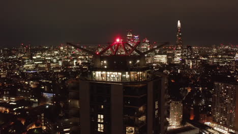 Fly-around-roof-lookout-terrace-at-tall-apartment-building.-Night-scene-with-city-panorama.-London,-UK