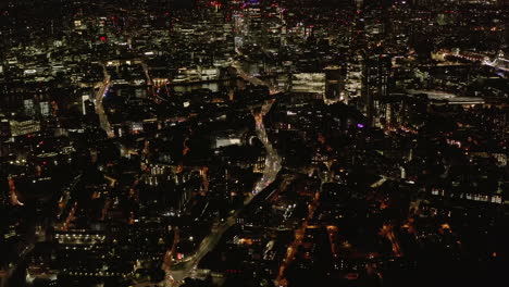 Fly-above-night-city.-Tilt-up-reveal-of-modern-skyscrapers-in-City-financial-hub.-Aerial-scene-with-city-lights.-London,-UK