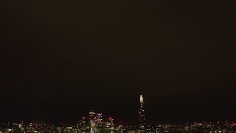 Tilt-down-reveal-of-night-city-skyline.-Modern-high-rise-business-buildings-glowing-into-dark.-London,-UK