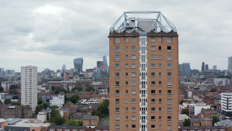 Orbit-shot-around-Winterton-House.-Tall-apartment-building-with-brick-facade.-Downtown-skyscrapers-in-background.-London,-UK