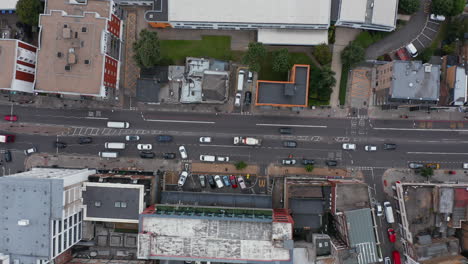 Aerial-birds-eye-overhead-top-down-descending-view-of-vehicles-driving-on-street-in-city.-Cars-going-out-from-parking-lot.-London,-UK