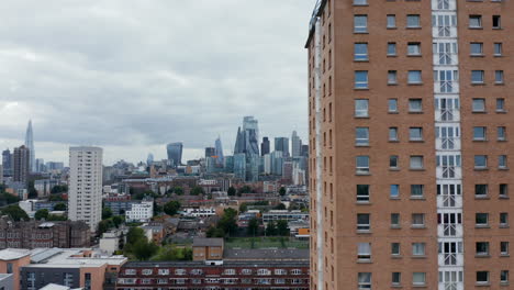 Descending-footage-of-Winterton-House.-High-rise-apartment-building-with-brick-facade.-Modern-tall-office-buildings-in-background.-London,-UK