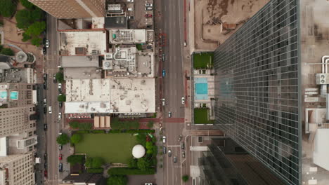 Aerial-birds-eye-overhead-top-down-view-of-wide-multi-lane-downtown-street-leading-between-skyscrapers.-Vertically-panning-view.-Dallas,-Texas,-US