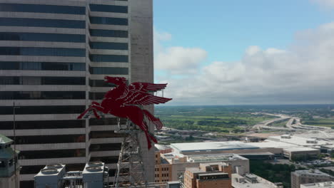 Drone-aerial-view-of-Pegasus-on-roof-of-Magnolia-Building.-Flying-around-two-massive-red-sculptures-perched-on-top-tall-building.-Dallas,-Texas,-US