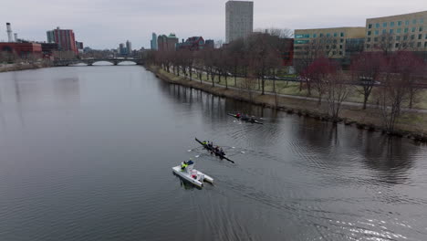 Sportsmen-sitting-in-rowing-boats-on-Charles-river-water-surface-and-waiting.-Busy-road-and-buildings-in-city-in-background.-Boston,-USA