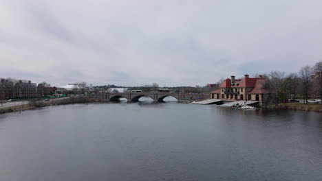Winter-or-early-spring-landscape-in-city.-Forwards-fly-above-Charles-river-at-Weld-Boat-House.-Vehicles-driving-on-Anderson-Memorial-Bridge.-Boston,-USA