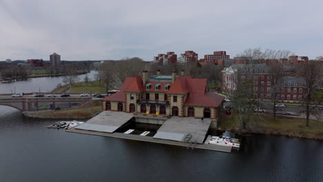 Slide-and-pan-shot-of-Weld-Boat-House-on-Charles-river-waterfront.-Vehicles-driving-on-road-and-old-Anderson-Memorial-Bridge.-Boston,-USA