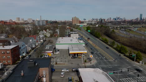Orbit-shot-around-of-gas-station-on-corner.-Vehicles-passing-through-road-intersection-in-urban-neighbourhood.-Boston,-USA