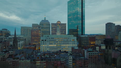 Tall-office-downtown-buildings-with-lighted-windows-at-twilight.-Forwards-fly-above-city.-Boston,-USA