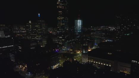 Backwards-reveal-of-high-rise-buildings-in-city-centre.-Fly-above-urban-borough-at-night.-Boston,-USA