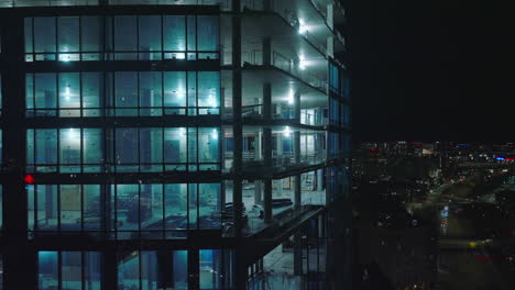 Descending-shot-along-brightly-illuminated-construction-site-of-modern-high-rise-building-at-night.-Boston,-USA