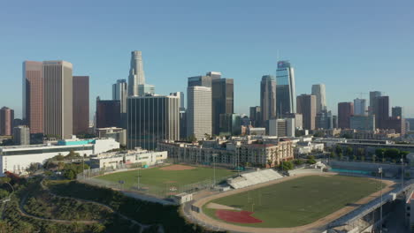 Estadio-Deportivo-Vacío-Por-El-Horizonte-De-La-Ciudad,-Muñeca-Aérea-En-Rascacielos-Reveladores-De-Los-ángeles,-California,-Estados-Unidos