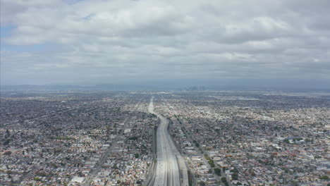 AERIAL:-Spectacular-View-over-Endless-City-Los-Angeles,-California-with-Big-Highway-Connecting-to-Downtown-on-Cloudy-Overcast-Day