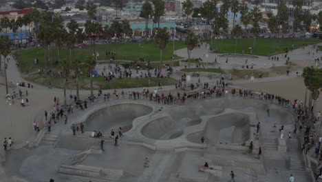Antena:-Sobre-El-Skatepark-De-Venice-Beach-Con-Visitantes-Y-Patinadores,-Patinaje,-Puesta-De-Sol,-Los-Angeles,-California