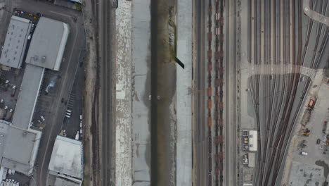 AERIAL:-Overhead-,-Birds-Eye-View-on-Los-Angeles-River-with-Water-on-Cloudy-Overcast-Sky-next-to-Train-Tracks