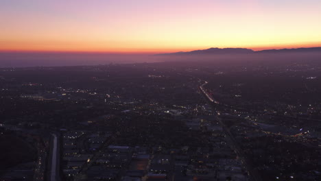 Aerial-Wide-view-of-Los-Angeles-and-Santa-Monica,-California-towards-pacific-ocean-from-Culver-City-at-Dusk,-Night-with-Purple-Sky-and-glowing-city-lights-with-Mountain-Silhouette