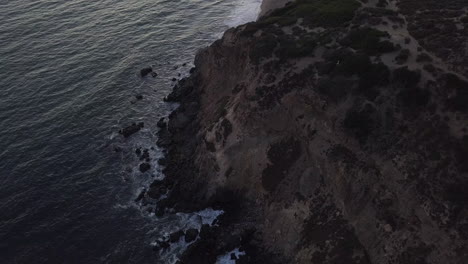 AERIAL:-flight-over-Malibu,-California-view-of-beach-Shore-Line-Pacific-ocean-at-sunset-with-mountain-cliff