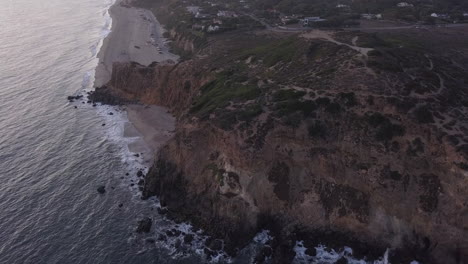 AERIAL:-flight-over-Malibu,-California-view-of-beach-Shore-Line-Pacific-ocean-at-sunset-with-mountain-cliff