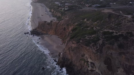 Mountains-at-Pacific-ocean-with-waves-crashing-on-cliff-in-Sunset-light,-Aerial-Wide-Angle
