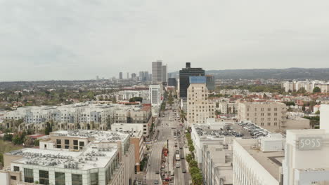 AERIAL:-Flight-over-Wilshire-Boulevard-close-to-Street-and-Buildings-with-Car-Traffic-in-Los-Angeles,-California-on-Overcast-Day