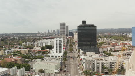 AERIAL:-Flight-over-Wilshire-Boulevard-close-to-Street-and-Buildings-with-Car-Traffic-in-Los-Angeles,-California-on-Overcast-Day