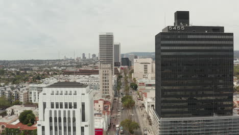AERIAL:-Flight-over-Wilshire-Boulevard-close-to-Street-and-Buildings-with-Car-Traffic-in-Los-Angeles,-California-on-Overcast-Day