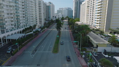 Forwards-tracking-of-vehicles-driving-on-multilane-trunk-road-in-modern-urban-borough.-Palm-trees-along-road.-Miami,-USA