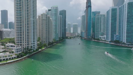 Breath-taking-view-of-boat-traffic-in-Miami-river-estuary-surrounded-by-modern-high-rise-buildings.-Forwards-fly-along-luxury-residential-towers.-Miami,-USA