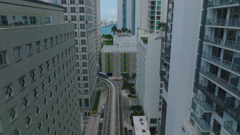 Aerial-ascending-footage-of-rail-car-driving-on-tracks-leading-between-high-rise-buildings.-Futuristic-concept-of-passenger-transport.-Miami,-USA
