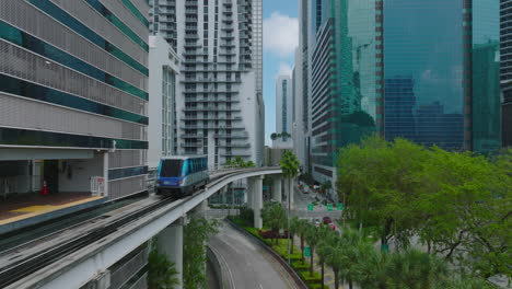 Forwards-tracking-of-Metromover-car-driving-on-elevated-track-surrounded-by-modern-downtown-skyscrapers.-Miami,-USA