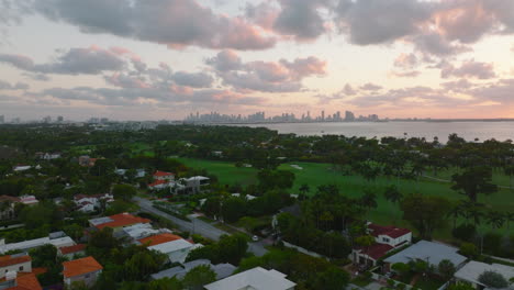 Luxurious-residences-and-golf-course-in-suburbs.-Skyline-with-skyscraper-silhouettes-against-sunset-sky-in-distance.-Miami,-USA