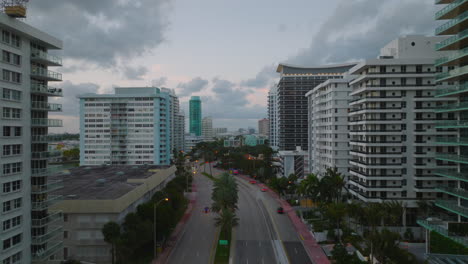Backwards-revealing-modern-buildings-along-multilane-trunk-road-in-city-at-twilight.-High-rise-apartment-buildings-with-balconies.-Miami,-USA