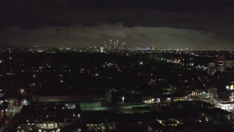 AERIAL:-Over-Dark-Hollywood-Los-Angeles-at-Night-with-Clouds-over-Downtown-and-City-Lights