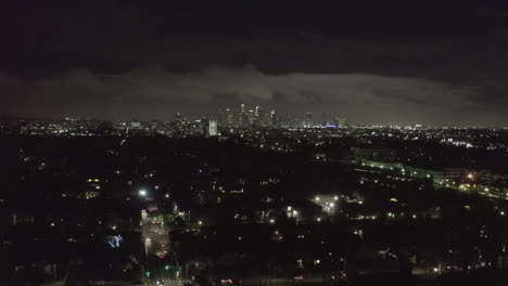 AERIAL:-Over-Dark-Hollywood-Los-Angeles-at-Night-with-Clouds-over-Downtown-and-City-Lights