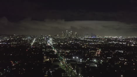 AERIAL:-Over-Dark-Hollywood-Los-Angeles-at-Night-with-Clouds-over-Downtown-and-City-Lights