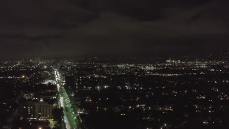 AERIAL:-Over-Dark-Hollywood-Los-Angeles-at-Night-view-on-Wilshire-Blvd-with-Clouds-over-Downtown-and-City-Lights