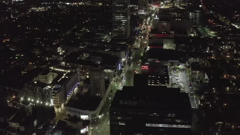 AERIAL:-Over-Wilshire-Boulevard-in-Hollywood-Los-Angeles-at-Night-with-Glowing-Streets-and-City-Car-Traffic-Lights