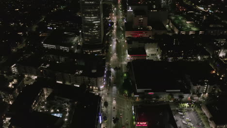 AERIAL:-Over-Wilshire-Boulevard-in-Hollywood-Los-Angeles-at-Night-with-Glowing-Streets-and-City-Car-Traffic-Lights