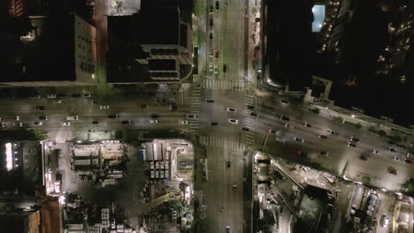 AERIAL:-Overhead-View-on-Intersection-Street-with-big-Construction-Site-and-Holes-in-Ground-at-Night-with-Glowing-Streets-and-City-Car-Traffic-Lights