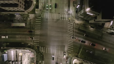 AERIAL:-Overhead-View-on-Intersection-Street-with-big-Construction-Site-and-Holes-in-Ground-at-Night-with-Glowing-Streets-and-City-Car-Traffic-Lights