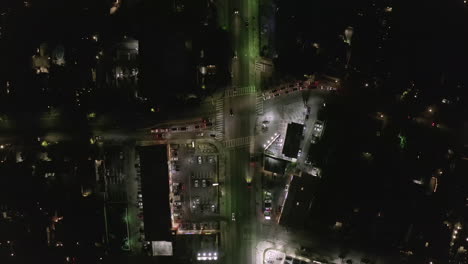 AERIAL:-Overhead-View-of-Street-at-Night-with-Store-Parking-Lot-and-City-Car-Traffic-Lights