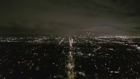 AERIAL:-View-over-Los-Angeles-at-Night-with-Wilshire-Boulevard-Glowing-Streets-and-City-Car-Traffic-Lights