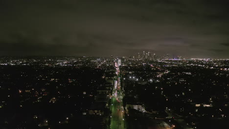 Antena:-Vista-De-Los-Ángeles-Por-La-Noche-Con-Las-Calles-Resplandecientes-Del-Bulevar-Wilshire-Y-Los-Semáforos-De-Los-Automóviles-De-La-Ciudad